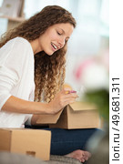 smiling young woman sitting on sofa unpacking received parcel. Стоковое фото, агентство Ingram Publishing / Фотобанк Лори