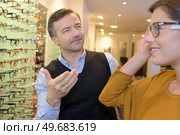 ophthalmologist and beautiful brunette female choosing glasses in optics store. Стоковое фото, агентство Ingram Publishing / Фотобанк Лори
