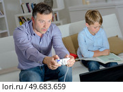 Father playing computer game, son reading book. Стоковое фото, агентство Ingram Publishing / Фотобанк Лори