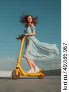 A woman in a blue dress is riding a yellow scooter. Стоковое AI-изображение, AI-художник Ярославский Максим / Фотобанк Лори