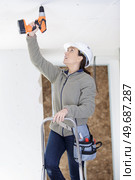 female drilling ceiling during home renovation. Стоковое фото, агентство Ingram Publishing / Фотобанк Лори