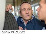 two mechanics car tyre pressure measuring. Стоковое фото, агентство Ingram Publishing / Фотобанк Лори