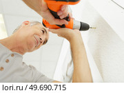 senior man drills a wall with a drill. Стоковое фото, агентство Ingram Publishing / Фотобанк Лори