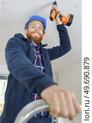 young man fixing drywall suspended ceiling using electrical screwdriver. Стоковое фото, агентство Ingram Publishing / Фотобанк Лори