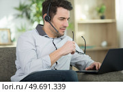 focused man in headset sit on couch working at laptop. Стоковое фото, агентство Ingram Publishing / Фотобанк Лори