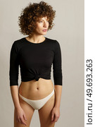 Side view of serious young female model standing and looking away at unseen illuminating lights reflecting on face against gray background. Slim woman in underwear standing against gray backdrop. Стоковое фото, агентство Ingram Publishing / Фотобанк Лори