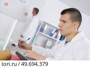 student wearing labcoat using computer and taking notes. Стоковое фото, агентство Ingram Publishing / Фотобанк Лори