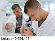 young scientist in uniform looking through a microscope. Стоковое фото, агентство Ingram Publishing / Фотобанк Лори