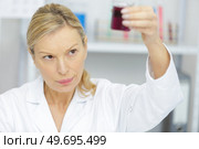 mature woman standing at a microscope and examining a flask. Стоковое фото, агентство Ingram Publishing / Фотобанк Лори