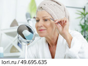 a senior woman plucking her eyebrows with tweezers. Стоковое фото, агентство Ingram Publishing / Фотобанк Лори