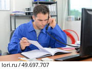 Builder checking through is notes over the phone. Стоковое фото, агентство Ingram Publishing / Фотобанк Лори