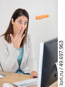 woman at office desk looks in surprise at dangling carrot. Стоковое фото, агентство Ingram Publishing / Фотобанк Лори