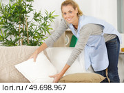 pleasant positive chambermaid tidying up a sofa. Стоковое фото, агентство Ingram Publishing / Фотобанк Лори