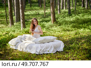 Woman wakes up in a summer forest. A girl drinks morning tea sitting on a mattress in the woods. Стоковое фото, агентство Ingram Publishing / Фотобанк Лори