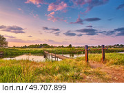 Landscape with sunset over river. Rural pedestrian old bridge. Evening with calm beautiful clouds on sky. Water reflection. Tranquil evening scene. Green filed and meadow. Europe, Belarus. Стоковое фото, агентство Ingram Publishing / Фотобанк Лори