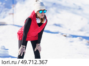 Young sportive female in sunglasses and vest leaning on knees while recovering breath after run in winter sunny nature. Sportswoman resting during jog in snowy terrain. Стоковое фото, агентство Ingram Publishing / Фотобанк Лори