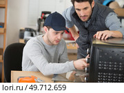 apprentice electrician working on appliance under supervision. Стоковое фото, агентство Ingram Publishing / Фотобанк Лори