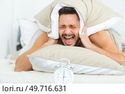 man covering ears with pillow to hide alarmclock noise. Стоковое фото, агентство Ingram Publishing / Фотобанк Лори