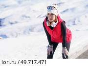 Focused athletic female in warm clothes and hat leaning forward while recovering breath after jog in winter road. Sportive female in outerwear having break in run. Стоковое фото, агентство Ingram Publishing / Фотобанк Лори