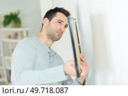 young man hanging a picture on the wall. Стоковое фото, агентство Ingram Publishing / Фотобанк Лори