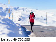 Full body of woman in outerwear and sunglasses jogging on asphalt road with snowy mountains. Female running on road in snowy mountains. Стоковое фото, агентство Ingram Publishing / Фотобанк Лори
