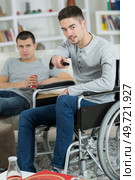 2 friends watching tv and drinking soda one is disabled. Стоковое фото, агентство Ingram Publishing / Фотобанк Лори