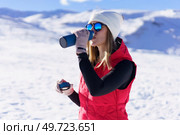 Side view of young female in warm clothes, beanie wool cap polarized sunglasses drinking warm water from thermos bottle and looking away while standing on snowy mountain slope in daylight. Young woman drinking water from bottle in highlands. Стоковое фото, агентство Ingram Publishing / Фотобанк Лори