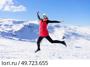 Full body of excited young female in vest cap, polarized sunglasses looking at camera while leaping up in air with stretched arms against snowy mountains and blue sky in daylight. Carefree young woman jumping and enjoying vacation on snowy slope. Стоковое фото, агентство Ingram Publishing / Фотобанк Лори