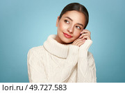 Portrait of young happy beautiful woman smiling and looking away, isolated on blue background in a warm white sweater. Concept of winter promo sale. Стоковое фото, агентство Ingram Publishing / Фотобанк Лори