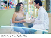 Side view of male positive druggist and glad woman looking at each other while sitting in pharmacy after measuring blood sugar. Happy pharmacist and patient during blood sugar test in pharmacy. Стоковое фото, агентство Ingram Publishing / Фотобанк Лори