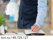 businessman standing at desk holding a safety helmet checks document. Стоковое фото, агентство Ingram Publishing / Фотобанк Лори