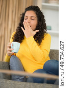 young lady on the sofa holding a cup and yawning. Стоковое фото, агентство Ingram Publishing / Фотобанк Лори
