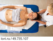 Top view of female physiotherapist massaging head for patient lying on couch during osteopathy session in light clinic. Female osteopath doing physiological and emotional therapy. Стоковое фото, агентство Ingram Publishing / Фотобанк Лори