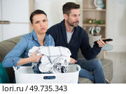 woman is fed up sorting laundry while partner watches television. Стоковое фото, агентство Ingram Publishing / Фотобанк Лори