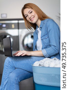 portrait of young woman holding digital tablet sitting at laundromat. Стоковое фото, агентство Ingram Publishing / Фотобанк Лори