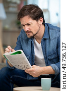 young man sitting doing a crossword puzzle looking thoughtfully. Стоковое фото, агентство Ingram Publishing / Фотобанк Лори