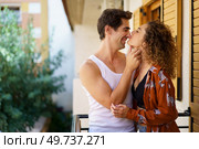 Side view of young romantic couple in casual clothes caressing gently while spending time together on balcony at modern apartment against blurred background. Romantic young couple caressing on balcony of modern building. Стоковое фото, агентство Ingram Publishing / Фотобанк Лори