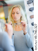 portrait of unsure female customer trying spectacles in optical store. Стоковое фото, агентство Ingram Publishing / Фотобанк Лори