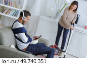 woman vacuuming while injured man is resting on a couch. Стоковое фото, агентство Ingram Publishing / Фотобанк Лори