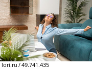 Young female freelancer in eyeglasses and smart casual stretching arms while working on laptop at table in living room at home. Happy woman stretching arms near laptop at home. Стоковое фото, агентство Ingram Publishing / Фотобанк Лори