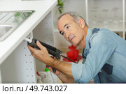 mature plumber fills the seam between the sink and furniture. Стоковое фото, агентство Ingram Publishing / Фотобанк Лори