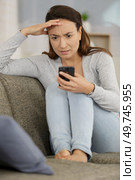 worried lady on sofa in front of smartphone. Стоковое фото, агентство Ingram Publishing / Фотобанк Лори