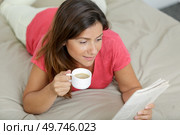 woman layed on bed with a coffee reading a newspaper. Стоковое фото, агентство Ingram Publishing / Фотобанк Лори