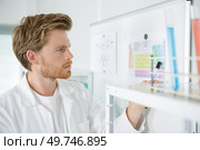 Man in labcoat looking at charts on white board. Стоковое фото, агентство Ingram Publishing / Фотобанк Лори