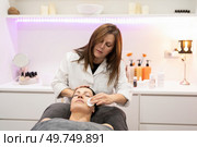 Beauty specialist removing cosmetic cream on face of female customer with skin care cotton pad while working in modern salon. Beautician cleaning face of woman with cotton pad in beauty salon. Стоковое фото, агентство Ingram Publishing / Фотобанк Лори