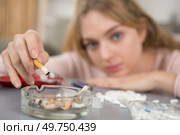 young lady holding a stubbed cigarette over an ashtray. Стоковое фото, агентство Ingram Publishing / Фотобанк Лори