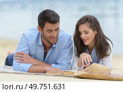 mid-adult couple layed on the beach looking at book. Стоковое фото, агентство Ingram Publishing / Фотобанк Лори