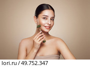 Close up video of a young woman looking relaxed and smiling while using a natural jade face roller. Facial treatment for anti aging and cosmetic cleaning with a derma roller. Стоковое фото, агентство Ingram Publishing / Фотобанк Лори