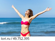 Content female with closed eyes in pink swimsuit raising arms and smiling while sunbathing and resting against blue sky and waving sea on summer holiday. Cheerful slim woman in bikini with raised arms. Стоковое фото, агентство Ingram Publishing / Фотобанк Лори