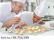 female pastry intern putting topping on coconut macaron. Стоковое фото, агентство Ingram Publishing / Фотобанк Лори